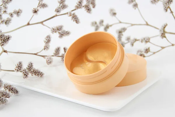 Çiçeklerin yanındaki beyaz arka planda hidrojel altın göz bantları. Kozmetoloji, özbakım, sağlık hizmetleri.