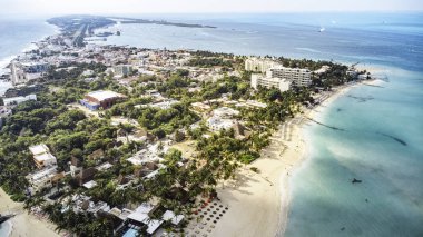 Isla Mujeres, Cancun, Mexico - Palmiye ağaçları ve arka planda bir şehir olan plaj. Sahil insanlarla dolu ve birçok şemsiye var.