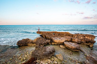 Isla Mujeres, Cancun, Meksika Rocky plajı okyanusa bakan bir çıkıntının üzerinde duran bir adam. Gökyüzü mavi ve su sakin.