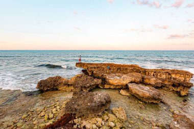 Isla Mujeres, Cancun, Meksika kayanın üzerinde duran bir adamla Rocky sahilleri. Gökyüzü mavi ve su sakin.