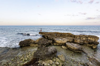 Isla Mujeres, Cancun, Meksika kayanın üzerinde duran bir adamla Rocky sahilleri. Gökyüzü mavi ve su sakin.