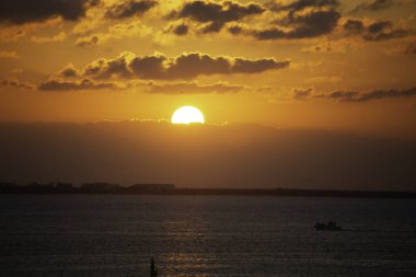 Isla Mujeres, Cancun, Meksika - Güneş okyanusun üzerinde batıyor, suyun üzerine sıcak bir parıltı saçıyor. Bir tekne uzaktan görülebilir ve gökyüzü bulutlarla doludur. Huzurlu ve huzurlu bir sahne.
