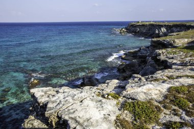 Isla Mujeres, Cancun, Mexico The ocean is calm and the shoreline is rocky. The water is a deep blue color. The sky is clear and bright
