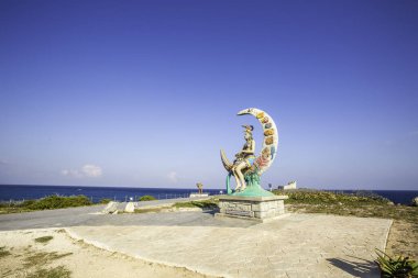 Mujeres Adası, Cancun, Meksika heykeli. Ay şeklinde büyük bir yapıda oturan bir kadın. Heykel kumlu bir sahil ve okyanusla çevrilidir. Sahne sakin ve huzurlu, kadın ve ayın yarattığı huzur ve sükunet duygusu