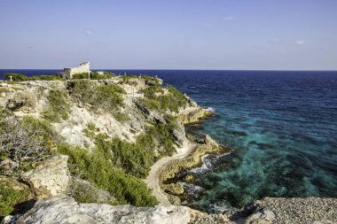 Isla Mujeres, Cancun, Mexico Beautiful blue ocean with a rocky shoreline and a small building in the distance. The scene is peaceful and serene, with the water and rocks creating a calming atmosphere