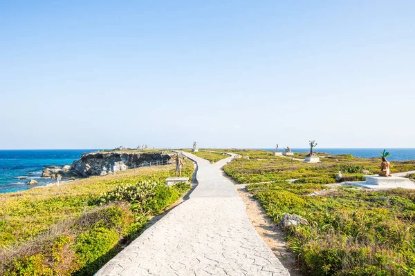 Isla Mujeres, Cancun, Meksika Yolu yemyeşil bir tarlada esiyor. Arka planda okyanus manzarası var. Sahne huzurlu ve sakin, dalgaların sesi uzaktan çarpıyor.