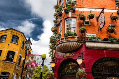 Londra, City, İngiltere, üzerinde yeşil işaret olan kırmızı bina. Binanın üzerinde bir sürü saksı bitkisi var.