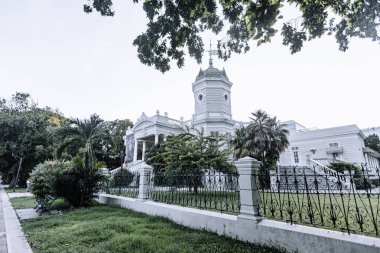 Merida, Yucatan, Meksika, üzerinde yeşil çitleri ve beyaz haçı olan büyük beyaz bir bina. Bina ağaçlarla çevrili ve yemyeşil bir çimenliği var. Sahnenin huzurlu ve huzurlu bir atmosferi var.