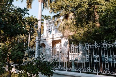 Merida, Yucatan, Meksika, önünde demir çitleri ve büyük bir ağacı olan beyaz ev. Evin bir balkonu ve merdiveni var, oraya doğru gidiyor. Çit süslenmiş ve ağaç yemyeşil. Huzur dolu bir sahne.