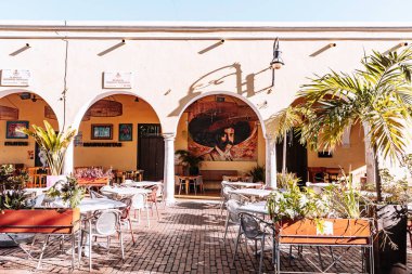 Merida, Yucatan, Meksika, avlu duvarında duvar resmi, masalar ve sandalyelerle. Avlu dışarıya açıktır ve tropikal bir havası vardır.