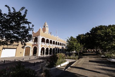 Merida, Yucatan, Meksika, saat kulesi ve geniş kemerli bir bina. Bina pembe ve üzerinde beyaz bir tabela var. Gökyüzü mavi ve berrak