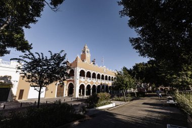 Merida, Yucatan, Meksika, saat kulesi ve geniş kemerli bir bina. Bina pembe ve bir sürü penceresi var. Gökyüzü mavi ve arka planda ağaçlar var.