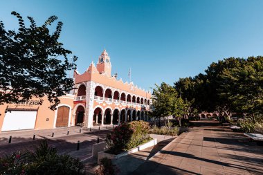 Merida, Yucatan, Meksika, saat kulesi ve geniş kemerli bir bina. Bina pembe ve üzerinde beyaz bir tabela var. Gökyüzü mavi ve berrak