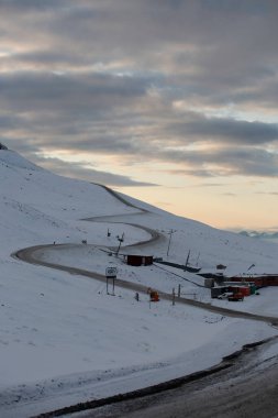 Longyerbeyen, Svalbard, küçük bir köye giden yolu olan Karlı Dağ. Gökyüzü bulutlu ve güneş batıyor.