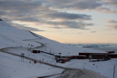 Longyerbeyen, Svalbard, Karlı Dağ küçük bir kasabaya giden bir yol. Gökyüzü bulutlu ve güneş batıyor.