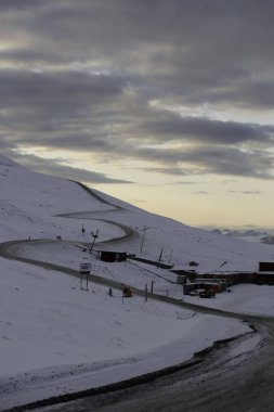 Longyerbeyen, Svalbard, Karlı Dağ küçük bir kasabaya giden bir yol. Gökyüzü bulutlu ve güneş batıyor.