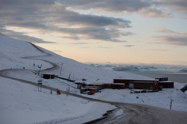 Longyerbeyen, Svalbard, uzakta kırmızı bir binası olan Karlı Dağ. Bina karla çevrili ve o bir pansiyon. Gökyüzü bulutlu ve güneş batıyor, kasvetli bir atmosfer yaratıyor.