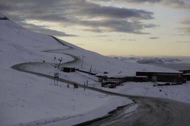Longyerbeyen, Svalbard, Karlı Dağ kırmızı bir binaya giden bir yol. Yol karla kaplı ve bina karla çevrili.