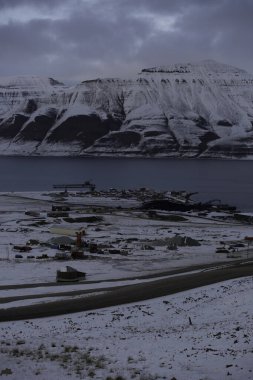 Longyerbeyen, Svalbard, Karlı dağ sıraları ve uzak bir kasaba. Gökyüzü bulutlu ve güneş batıyor.