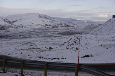 Longyerbeyen, Svalbard, yol kenarında kırmızı ve beyaz işareti olan Karlı dağ sıraları. Yol boş ve yol kenarına yığılmış kar var.