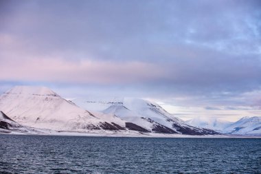 Longyerbeyen, Svalbard, arkasında mavi bir okyanus olan güzel dağ sırası. Gökyüzü bulutlu ve güneş batıyor.