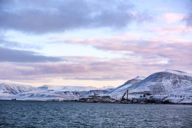 Longyerbeyen, Svalbard, arkasında sakin mavi bir okyanus olan karlı bir dağ manzarası. Gökyüzü bulutlarla dolu. Huzurlu ve huzurlu bir atmosfer yaratıyor.