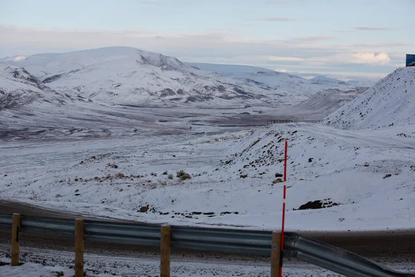 Longyerbeyen, Svalbard, yol kenarında kırmızı ve beyaz işareti olan Karlı dağ sıraları. Yol boş ve yol kenarına yığılmış kar var.