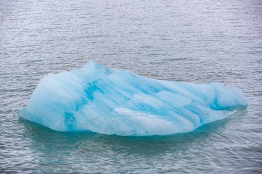 Svalbard seyahati. Okyanusta yüzen büyük bir buz parçası. Gökyüzü bulutlu ve su mavi.