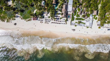 Tulum Sahili, Quintana Roo, Meksika, Sahilde birkaç kişi ve arka planda bir otel. Sahil sakin ve huzurlu, okyanus dalgaları yavaşça kıyıya vuruyor. Otel, doğal sörfçülere uyum sağlayan küçük, rahat bir işletme.