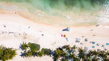 Bir sürü insan ve şemsiyeyle dolu bir plaj. Gökyüzü mavi ve su sakin.