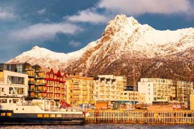 Svolvear, Lofoten Adası, Norveç Arkasında büyük bir dağ. Şehir binalarla dolu ve rıhtıma bir tekne yanaştı.