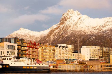 Svolvear, Lofoten Adası, Norveç Arkasında büyük bir dağ. Binalar yüksek ve rıhtıma yanaşmış bir tekne var.