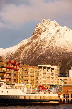 Svolvear, Lofoten Adası, Norveç sıradağları limana yanaşmış büyük kırmızı bir teknesi olan bir şehrin arka planında.