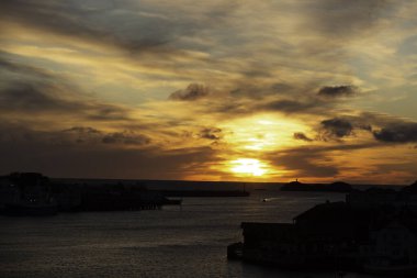 Svolvear, Lofoten Adası, Norveç Güneş suyun üzerinde batıyor, güzel ve sakin bir atmosfer yaratıyor. Gökyüzü bulutlarla dolu, sahnenin huzurunu artırıyor. Su sakin ve durgun, günbatımının renklerini yansıtıyor.