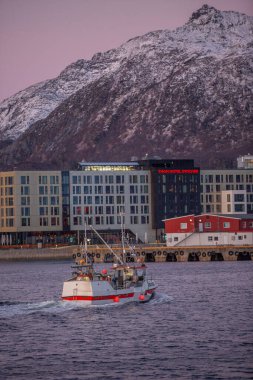 Svolvear, Lofoten Adası, Norveç. Tekne bir binanın yakınında okyanusta seyrediyor. Gökyüzü pembe ve su sakin.