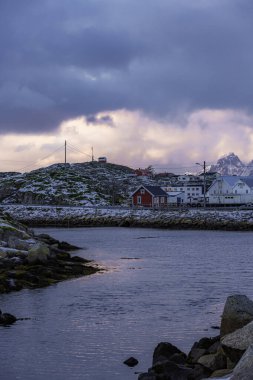 İçinden nehir akan küçük bir kasabanın güzel manzarası. Gökyüzü bulutlu ve güneş batıyor. Huzurlu ve huzurlu bir atmosfer yaratıyor.