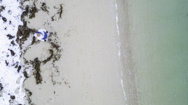 Sahilde yatan bir insan okyanusu seyrediyor. Kumsal yosunla kaplıdır ve su da güzel bir mavi tondur.