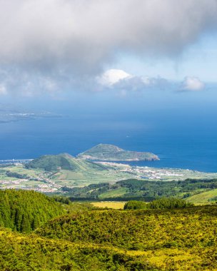 Faial, Azores Adaları, Portekiz. Arkasında mavi bir okyanus olan yeşil bir tepe manzarası. Gökyüzü bulutlu, ama görüntünün genel havası huzurlu ve huzurlu.