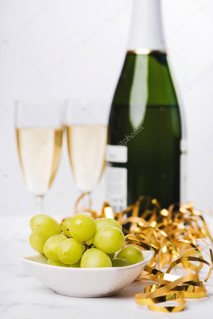 New Years Eve celebration concept background. Closeup of grapes with champagne bottle and two glasses blurred on the background on marble table. Selective focus,blurred background
