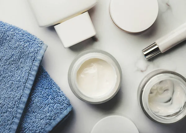 Skincare products.Cream jars,lotion, exfoliating cream and a blue towel on a marble  table