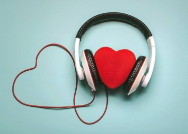 kalp kulaklığı ve kırmızı kalp şeklinde bir çatırtı mavi arka planda. Romantik müzik konsepti.