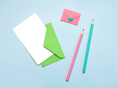 Beyaz kartlı yeşil kağıt zarf, pembe zarf pembe ve mavi arka planda yeşil kalemler.