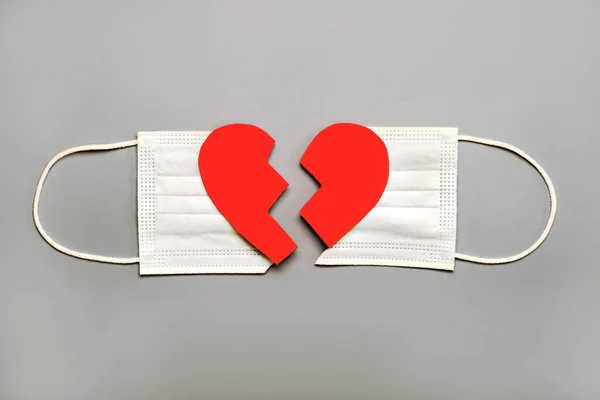 Protective surgical mask split in two with a broken heart on a gray background.Concept of divorce due to the 2019 coronavirus pandemic