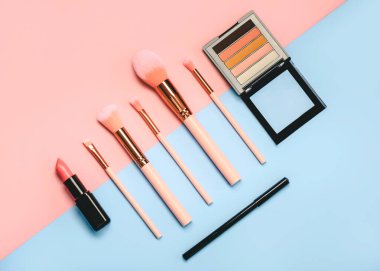 Pembe ve mavi arkaplanda farklı makyaj malzemeleri ve aksesuarlar. Makyaj Modası
