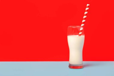 Bir bardak süt ve kırmızı beyaz pipet. Kırmızı ve mavi arka planda fotokopi alanı olan.
