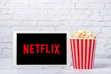 Beyaz bir dijital tabletin ekranındaki Netflix logosu beyaz tuğlaların arka planında patlamış mısır ile