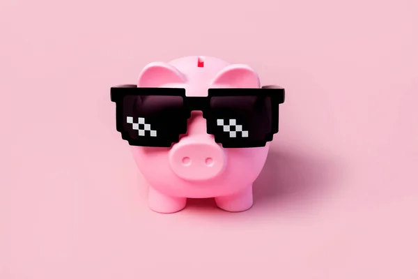 Pink piggy money bank with black sunglasses on a pink background