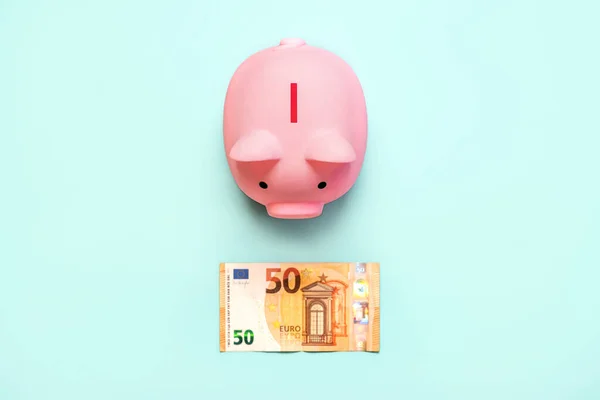 Top view of pink piggy money bank with euro bill on a blue background