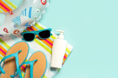 Yaz tatili kavramı. Mavi parmak arası terlikler, plaj havlusu, mavi güneş gözlüğü, bir şişe güneş kremi ve mavi arka planda fotokopi alanı.