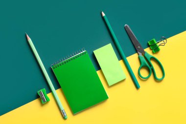 Sarmal not defteri ve okul malzemelerinin sarı ve yeşil arkaplandan üst görüntüsü